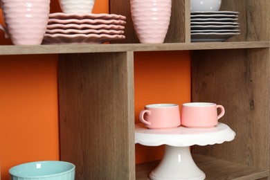 Photo of Shelving unit with different dishware and cups near orange wall indoors, closeup