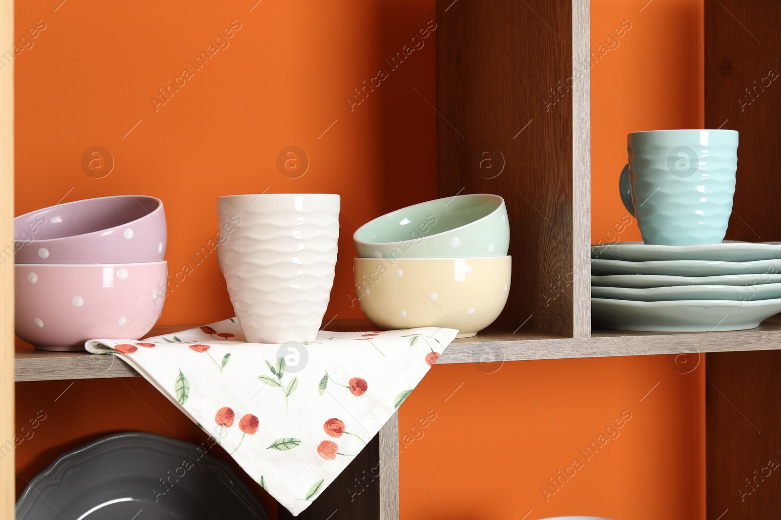 Photo of Shelving unit with different dishware and cups near orange wall indoors, closeup