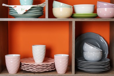 Photo of Shelving unit with different dishware and cups near orange wall indoors