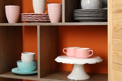 Photo of Shelving unit with different dishware and cups near orange wall indoors, closeup