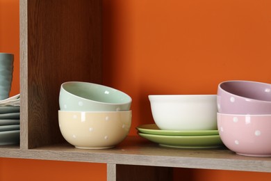 Photo of Different dishware on wooden shelf near orange wall indoors, closeup