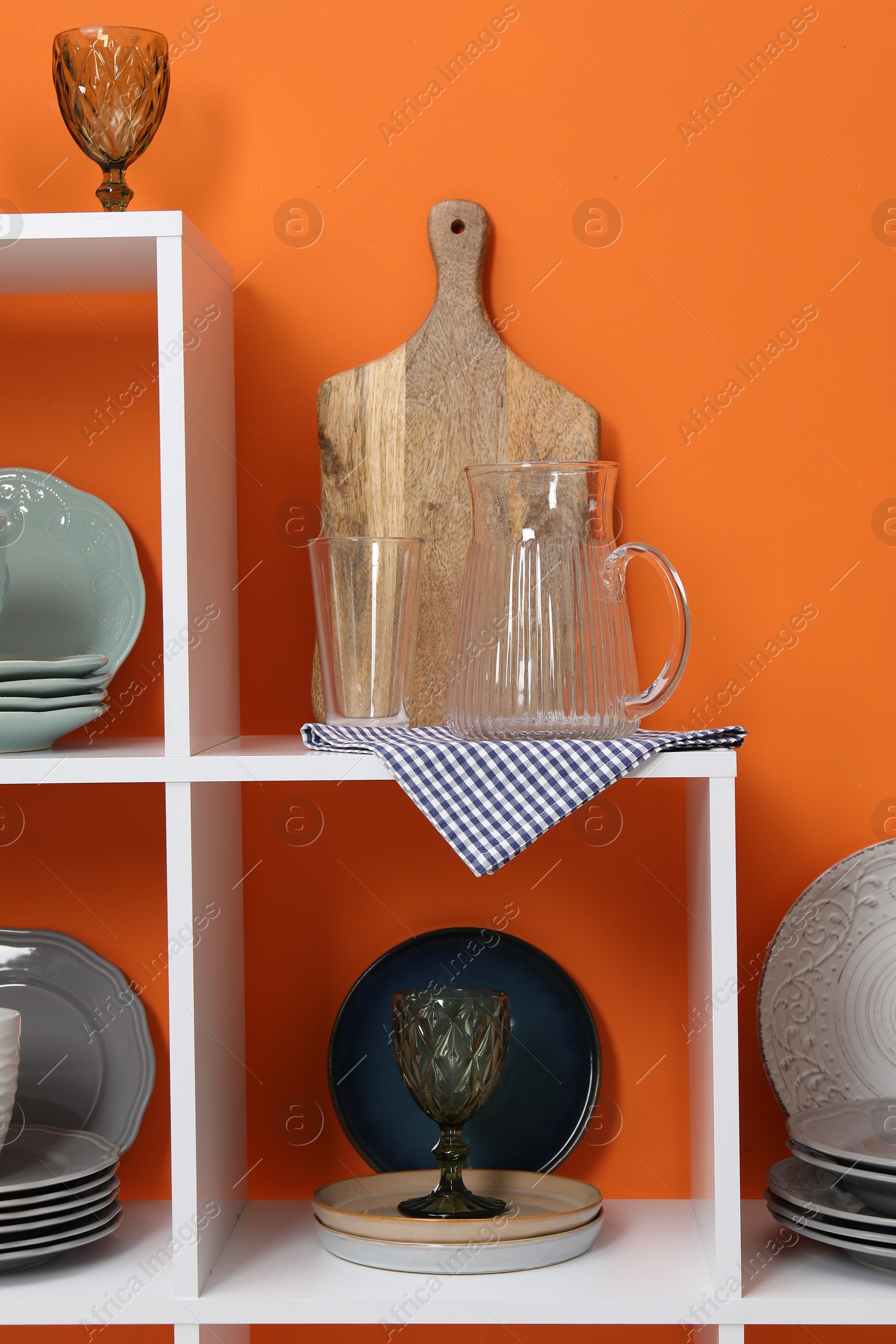 Photo of Shelving unit with different dishware and glasses near orange wall indoors