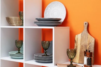 Photo of Shelving unit with different dishware and glasses near orange wall indoors