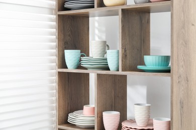 Photo of Shelving unit with different dishware and cups near white wall indoors