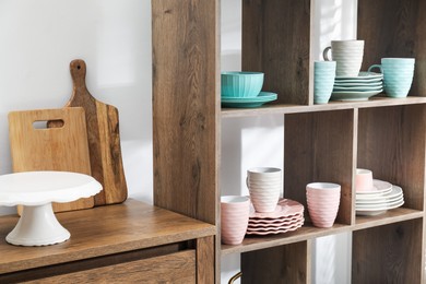 Photo of Shelving unit with different dishware and cups near white wall indoors