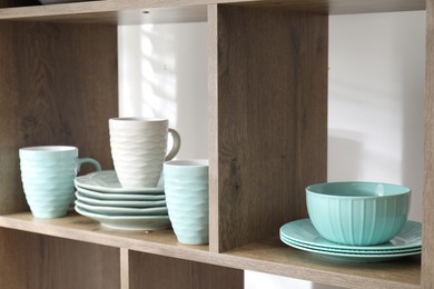 Photo of Different plates and cups on shelves near white wall indoors, closeup