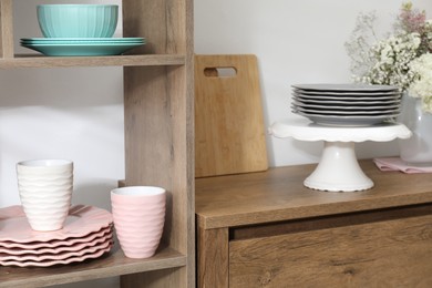 Photo of Shelving unit with different dishware and cups near white wall indoors