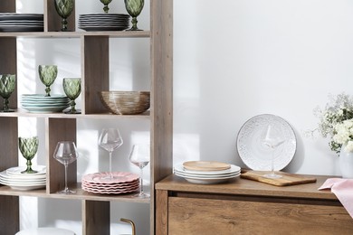 Photo of Shelving unit with different dishware and glasses near white wall indoors