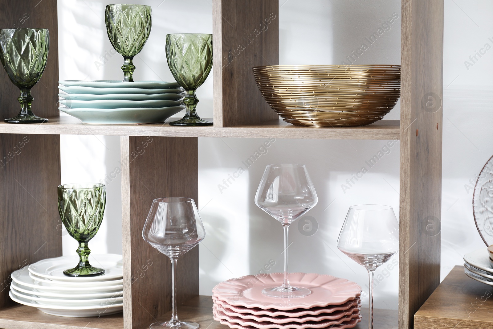 Photo of Shelving unit with different dishware and glasses near white wall indoors