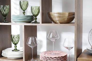 Photo of Shelving unit with different dishware and glasses near white wall indoors