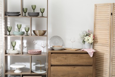 Photo of Shelving unit with different dishware and glasses near white wall indoors
