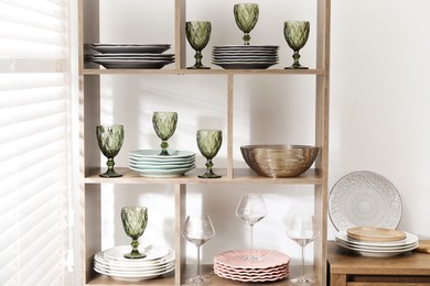 Photo of Shelving unit with different dishware and glasses near white wall indoors