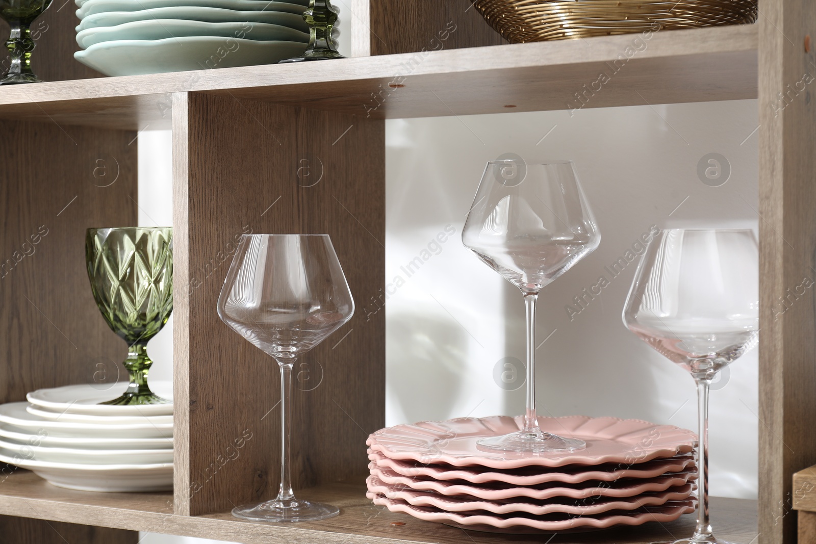 Photo of Different plates and glasses on wooden shelves near green white indoors, closeup