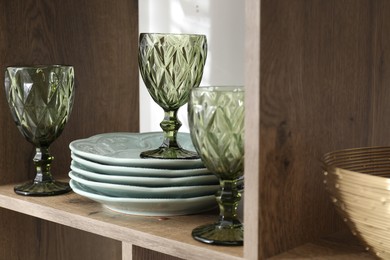 Photo of Different plates and glasses on wooden shelf indoors, closeup