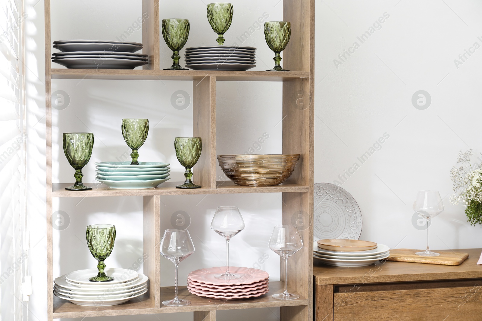 Photo of Shelving unit with different dishware and glasses near white wall indoors