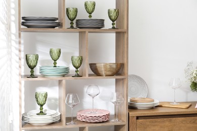 Photo of Shelving unit with different dishware and glasses near white wall indoors