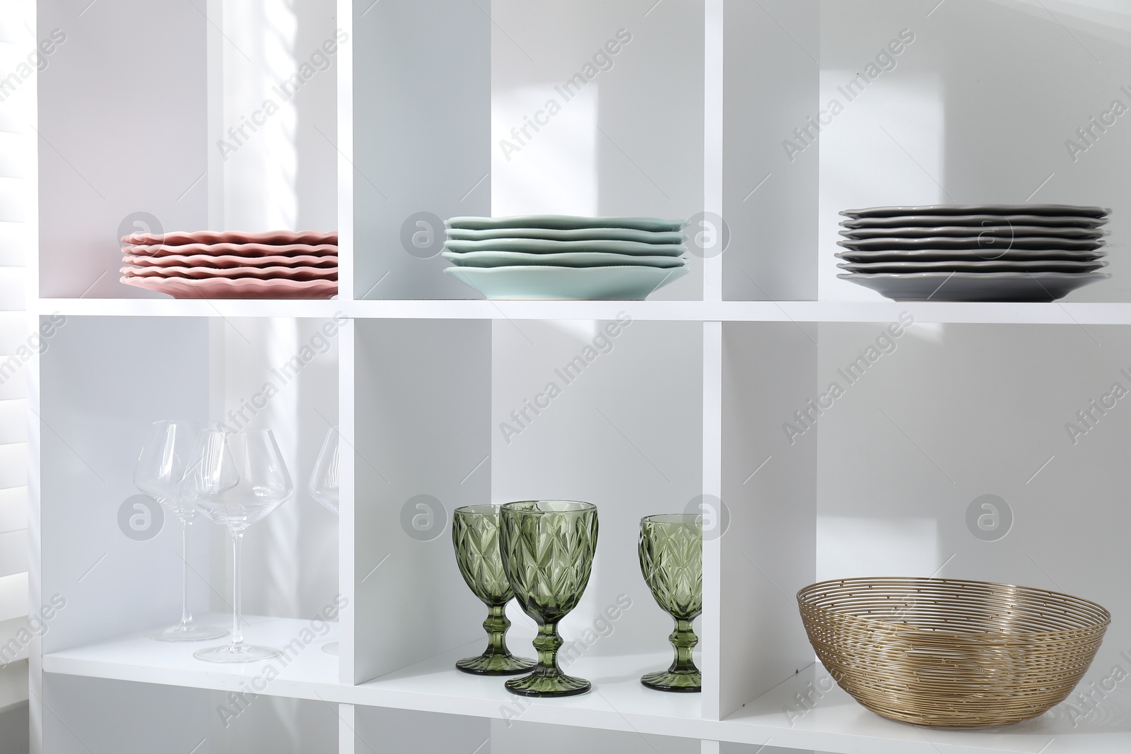 Photo of Shelving unit with different dishware and glasses near white wall indoors