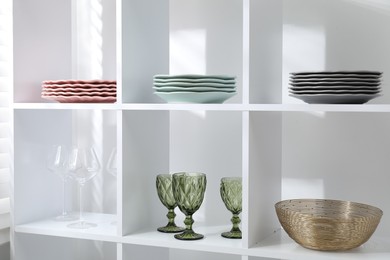 Photo of Shelving unit with different dishware and glasses near white wall indoors