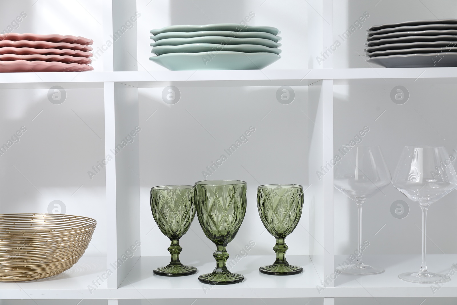 Photo of Shelving unit with different dishware and glasses near white wall indoors