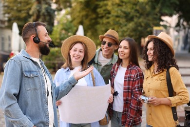 Photo of Guide with headset and group of tourists on city street during excursion