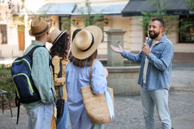 Photo of Guide with microphone and group of tourists on city street during excursion