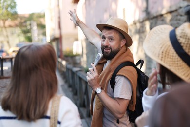 Photo of Guide with microphone and tourists on city street during excursion