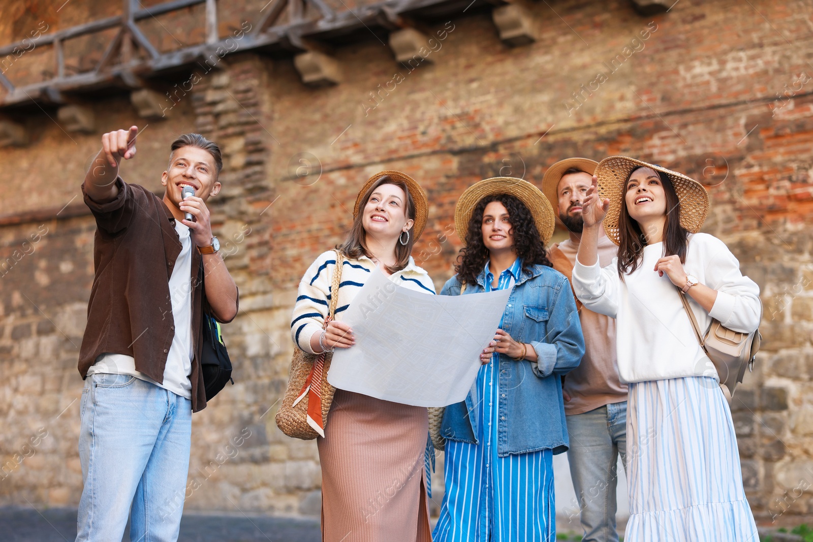 Guide with microphone and group of tourists on city street during excursion, low angle view Photo of Guide with microphone and group of tourists on city street during excursion, low angle view