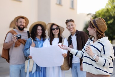 Photo of Guide with microphone and group of tourists on city street during excursion, selective focus
