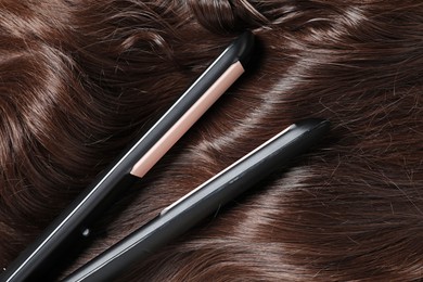 Photo of Modern flat iron on shiny brown hair, top view