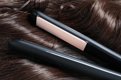 Photo of Modern flat iron on shiny brown hair, closeup