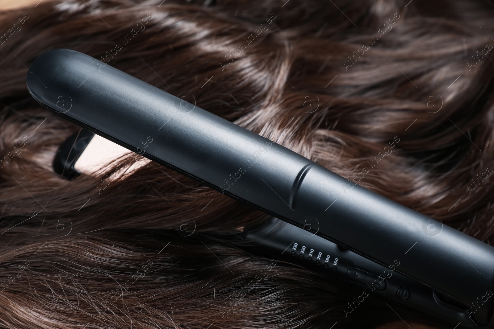 Modern flat iron on shiny brown hair, closeup Photo of Modern flat iron on shiny brown hair, closeup