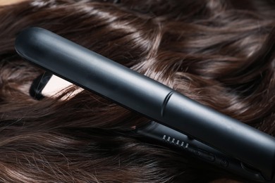 Photo of Modern flat iron on shiny brown hair, closeup