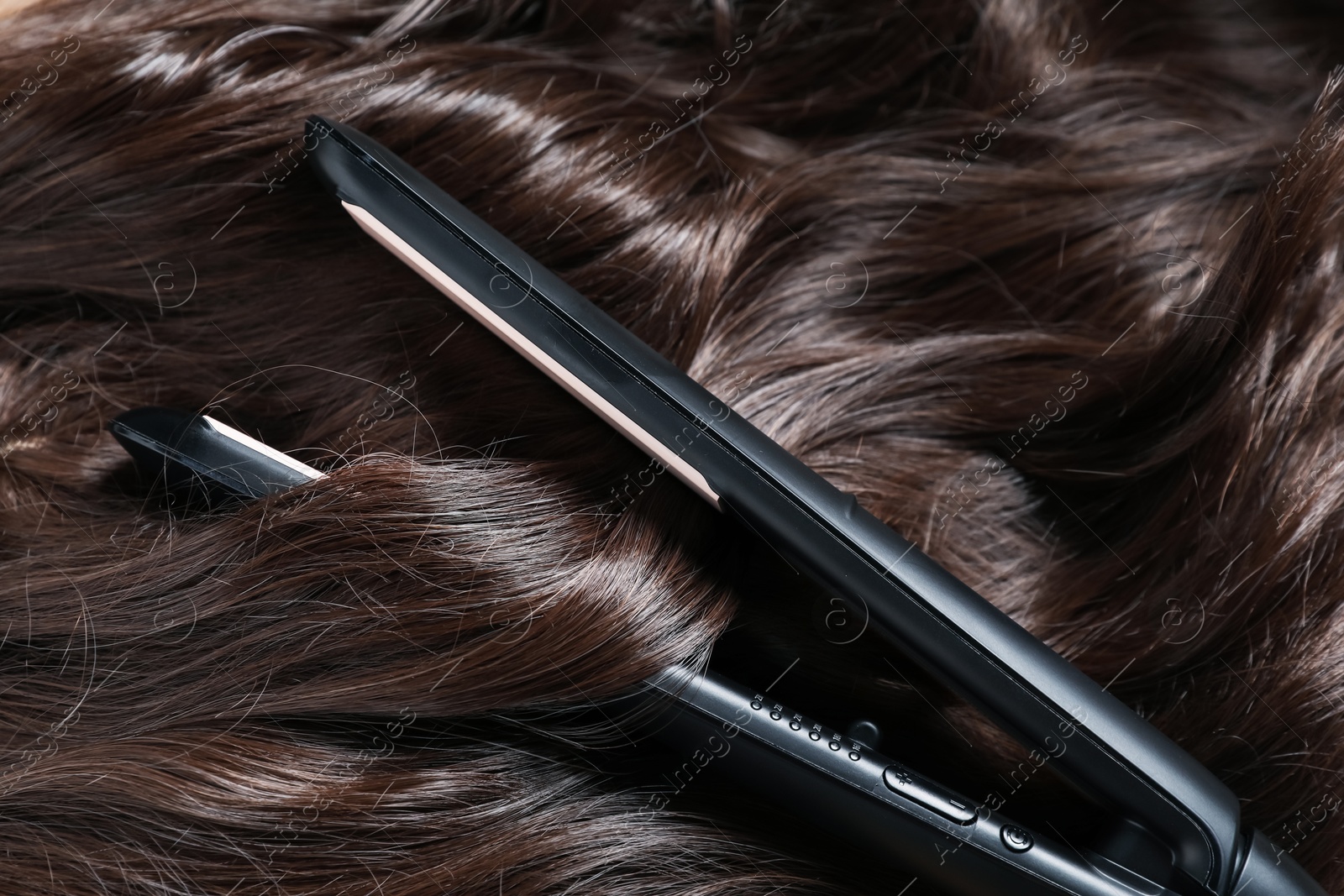 Modern flat iron on shiny brown hair, closeup Photo of Modern flat iron on shiny brown hair, closeup