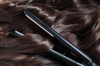 Photo of Modern flat iron on shiny brown hair, closeup
