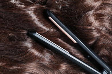 Photo of Modern flat iron on shiny brown hair, top view