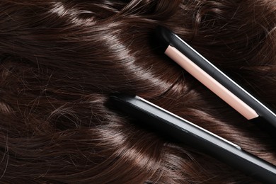 Photo of Modern flat iron on shiny brown hair, closeup