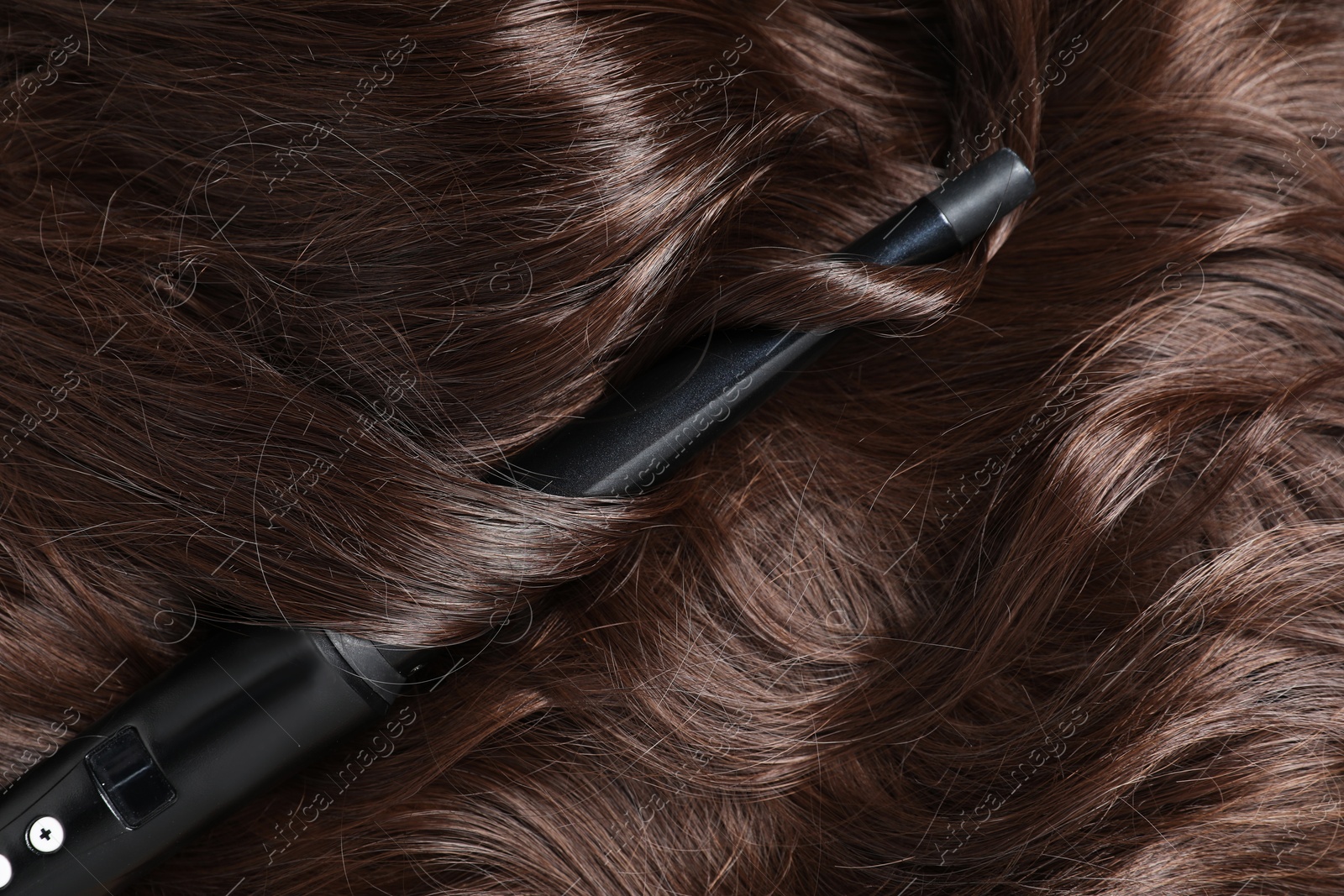 Photo of Curling iron with shiny brown hair, top view