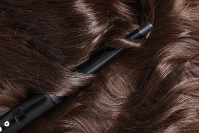 Photo of Curling iron with shiny brown hair, top view
