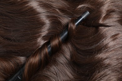 Photo of Curling iron with shiny brown hair, top view