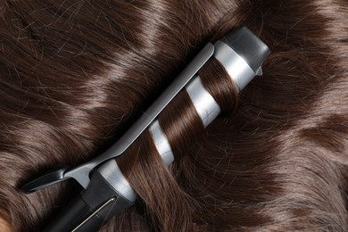 Photo of Curling iron with shiny brown hair, top view