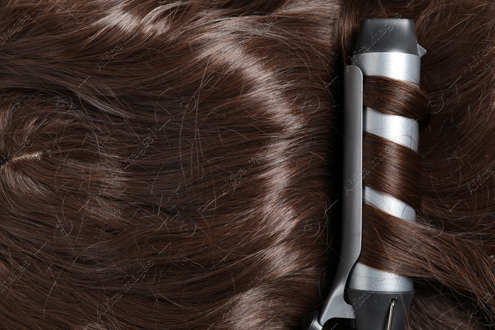 Curling iron with shiny brown hair, top view Photo of Curling iron with shiny brown hair, top view