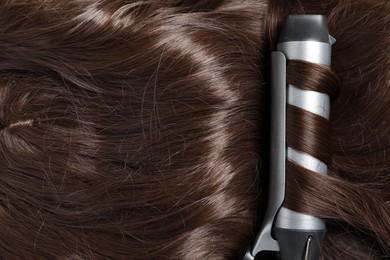 Photo of Curling iron with shiny brown hair, top view