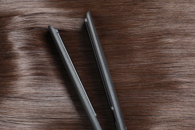 Photo of Modern flat iron on shiny brown hair, top view