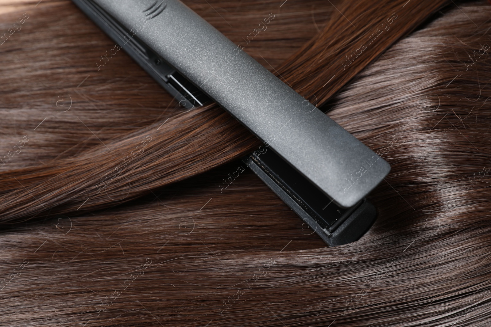 Modern flat iron with shiny brown hair, closeup Photo of Modern flat iron with shiny brown hair, closeup