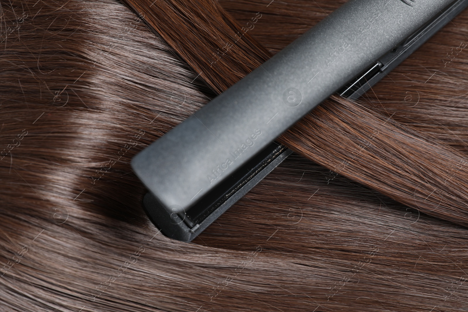 Photo of Modern flat iron with shiny brown hair, closeup