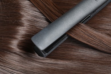 Photo of Modern flat iron with shiny brown hair, closeup