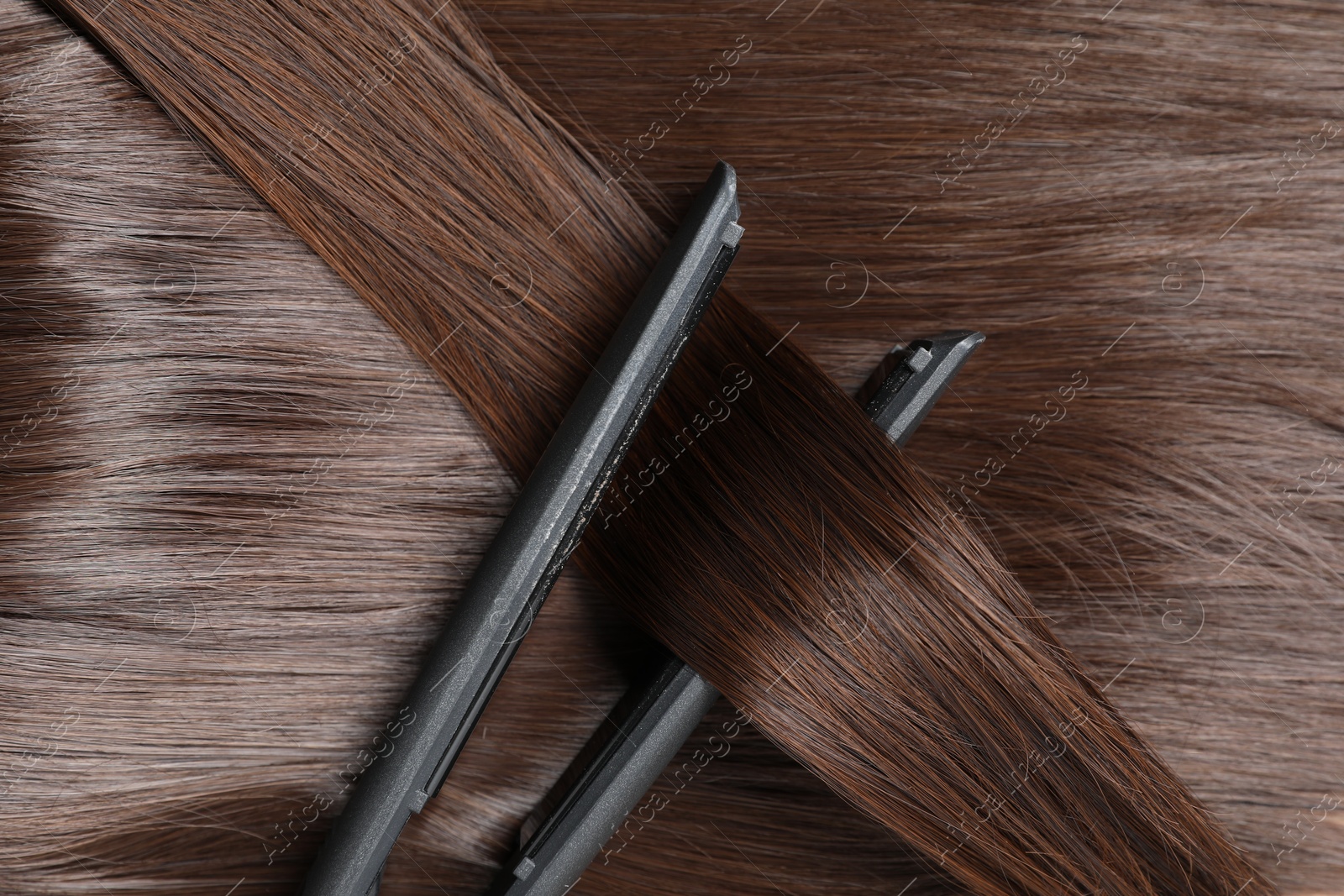 Photo of Modern flat iron with shiny brown hair, top view