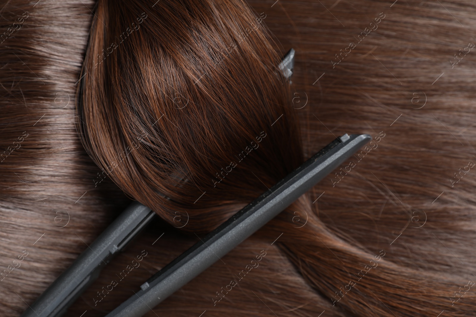 Photo of Modern flat iron with shiny brown hair, top view