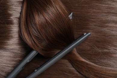 Photo of Modern flat iron with shiny brown hair, top view