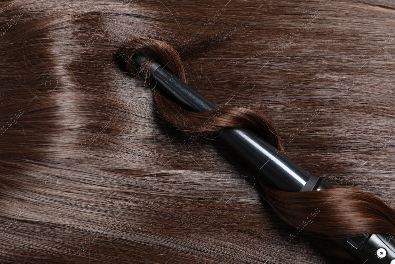 Curling iron with shiny brown hair, top view Photo of Curling iron with shiny brown hair, top view